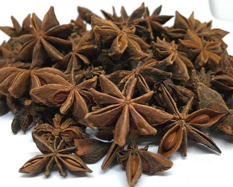 May include: A close-up image of a pile of dried star anise pods. The pods are brown and have a star shape with eight points. The pods are arranged in a random pattern.