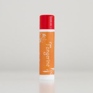 Puede incluir: Un tubo de bálsamo labial rojo y blanco con la palabra "Tangerine" impresa en la etiqueta. La etiqueta tiene un diseño floral.
