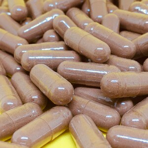 May include: A close-up image of a pile of brown capsules. The capsules are made of a clear material and contain a brown powder.