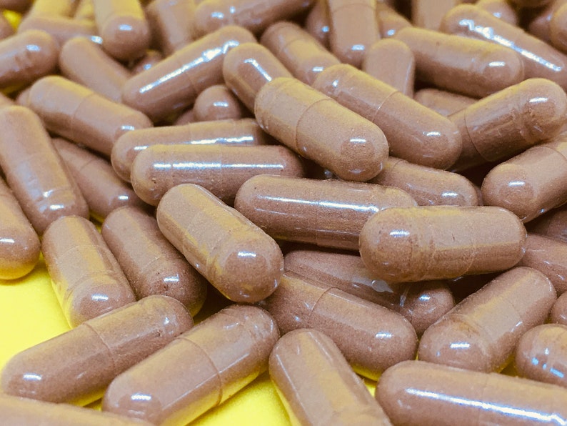 May include: A close-up image of a pile of brown capsules. The capsules are made of a clear material and contain a brown powder.