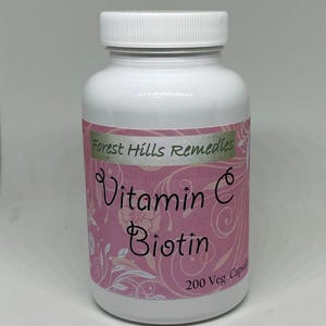 May include: A white plastic bottle with a white lid. The label is pink with the words "Vitamin C Biotin" and "Forest Hills Remedies". The bottle contains 200 capsules.