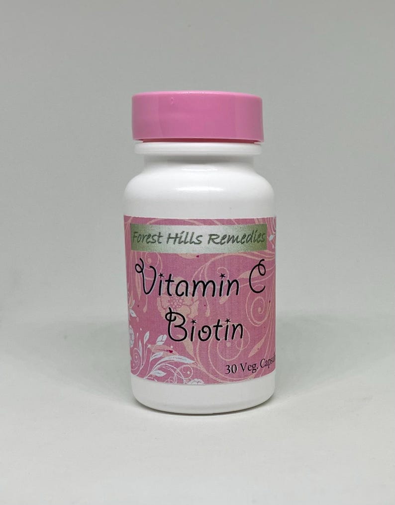 May include: A white bottle with a pink lid, labeled "Forest Hills Remedies." The label features the words "Vitamin C Biotin" in a decorative font, with a pink floral design. The bottle contains 30 capsules.