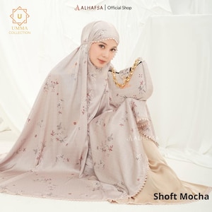 May include: A woman wearing a Shoft Mocha prayer garment and matching handbag. The light brown garment features a floral pattern and scalloped edges. The handbag has a gold chain strap. The image includes the text "UMMA COLLECTION" and "ALHAFSA | Official Shop."