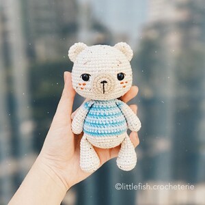 May include: A crocheted white bear wearing a blue and white striped shirt. The bear has a small, crocheted nose and embroidered eyes.