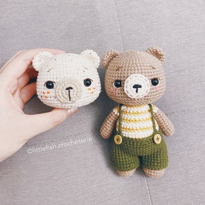 May include: Two crocheted stuffed bears. One is white with brown eyes and a brown nose. The other is brown with yellow and white striped clothing and a green vest.