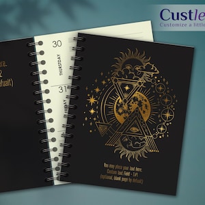 K&ouml;nnte beinhalten: Schwarzes Spiralnotizbuch mit goldenem Himmelsdesign auf dem Cover. Das Design umfasst Sonne, Mond, Sterne und geometrische Formen. Das Notizbuch hat linierte Seiten und Text, der lautet: "You may place your text here. Custom text Field - T#2 (optional, blank page by defualt)".