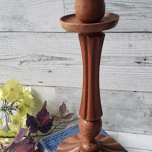 May include: A wooden candlestick, featuring a fluted stem and a round base. The candlestick is a warm brown colour and has a small cup-like holder at the top. It is displayed on antique books.