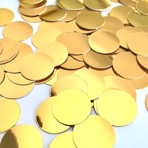 May include: A large pile of gold metallic round confetti circles. The circles are scattered on a white surface.