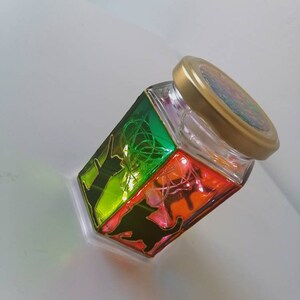 May include: A glass jar with a gold lid, decorated with a rainbow-colored design and black silhouettes of animals. The jar is filled with fairy lights.