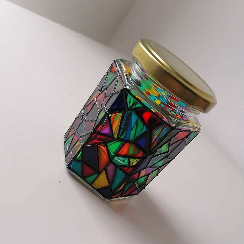 May include: A glass jar with a gold lid decorated with colorful geometric shapes and a stained glass effect.