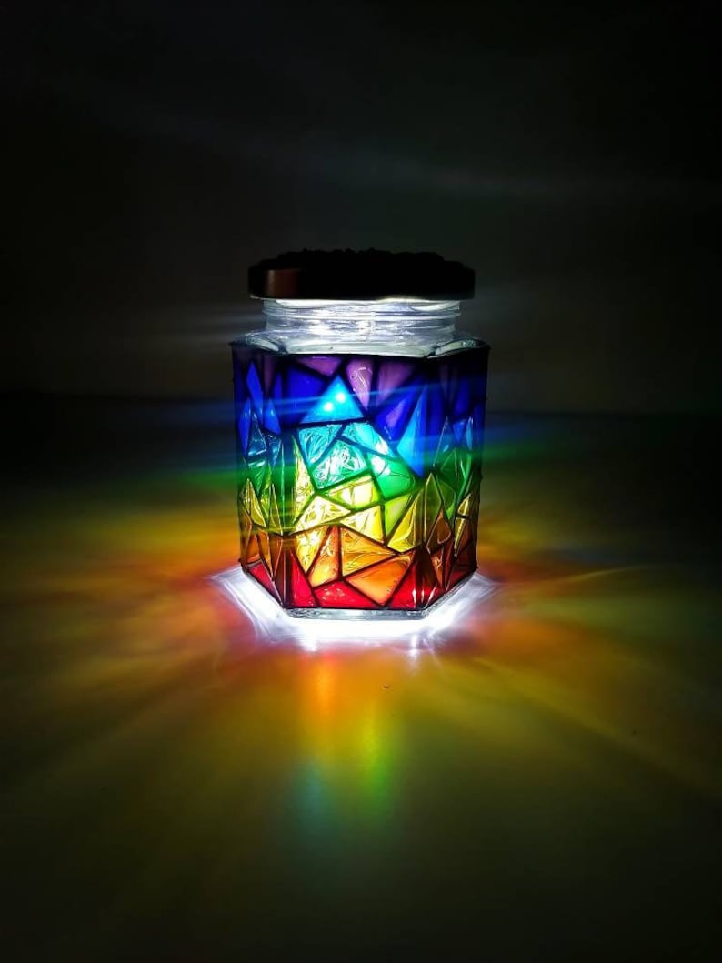 May include: A glass jar with a rainbow stained glass design, illuminated from within by a string of LED lights.