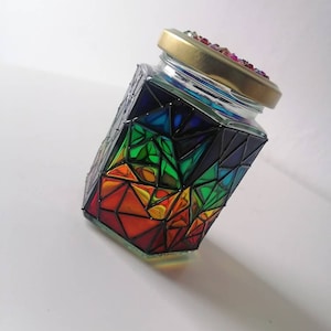 May include: A glass jar with a rainbow geometric design. The jar has a gold lid with colorful rhinestones.