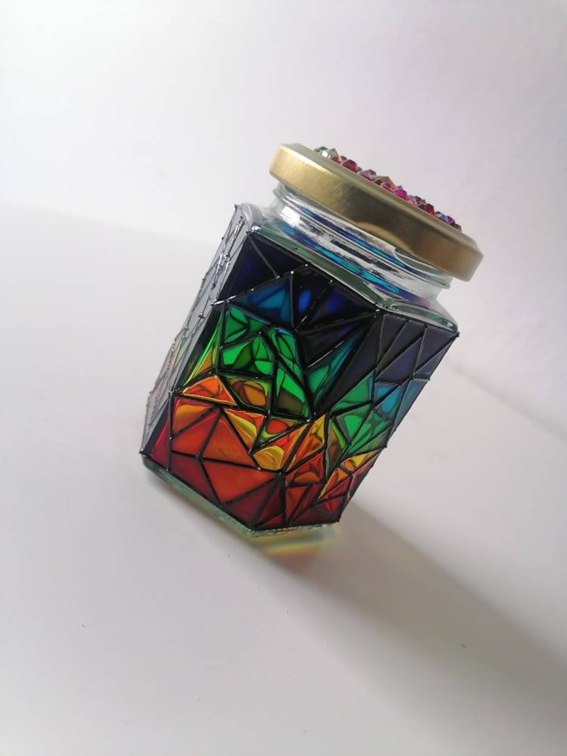May include: A glass jar with a rainbow geometric design. The jar has a gold lid with colorful rhinestones.