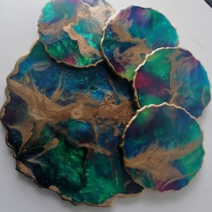 Peut inclure: Ensemble de cinq sous-verres ronds avec un design abstrait vert, bleu et or. Les sous-verres ont une bordure dorée et sont en résine.