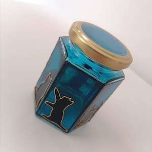 May include: A teal blue glass jar with a gold lid. The jar has black silhouettes of cats painted on the sides.