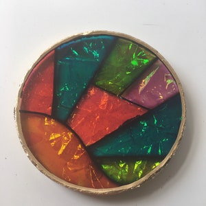 Könnte beinhalten: Ein runder, bunter, schillernder Untersetzer aus Harz mit goldfarbenem Rand. Der Untersetzer besteht aus mehreren Harzstücken, jedes mit einer anderen Farbe und einem anderen Muster. Die Farben umfassen Rot, Orange, Gelb, Grün, Blau und Lila.