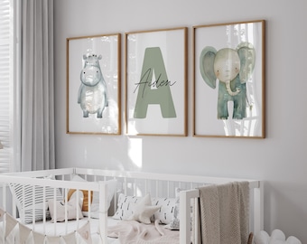 Könnte beinhalten: Drei gerahmte Drucke mit einem Aquarell-Design. Die Drucke zeigen ein Flusspferd, den Buchstaben A und einen Elefanten. Der Buchstabe A ist in hellgrün gehalten und der Name Aiden ist in schwarzer Schrift geschrieben. Die Drucke hängen an einer weißen Wand über einem weißen Kinderbett.