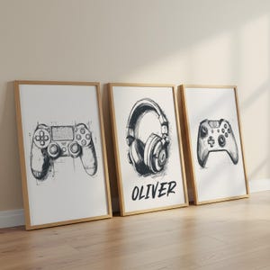 Pode incluir: Três impressões de arte emolduradas com tema de jogos. Cada impressão apresenta um esboço a preto e branco de um controlador de videogame, fones de ouvido e outro controlador. A impressão do meio tem o nome "OLIVER" em letras pretas em negrito.