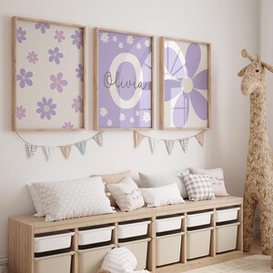 May include: Three framed prints with a purple and white floral design. The middle print has the name "Olivia" written in cursive. The prints are hanging on a white wall above a wooden storage bench with white bins.