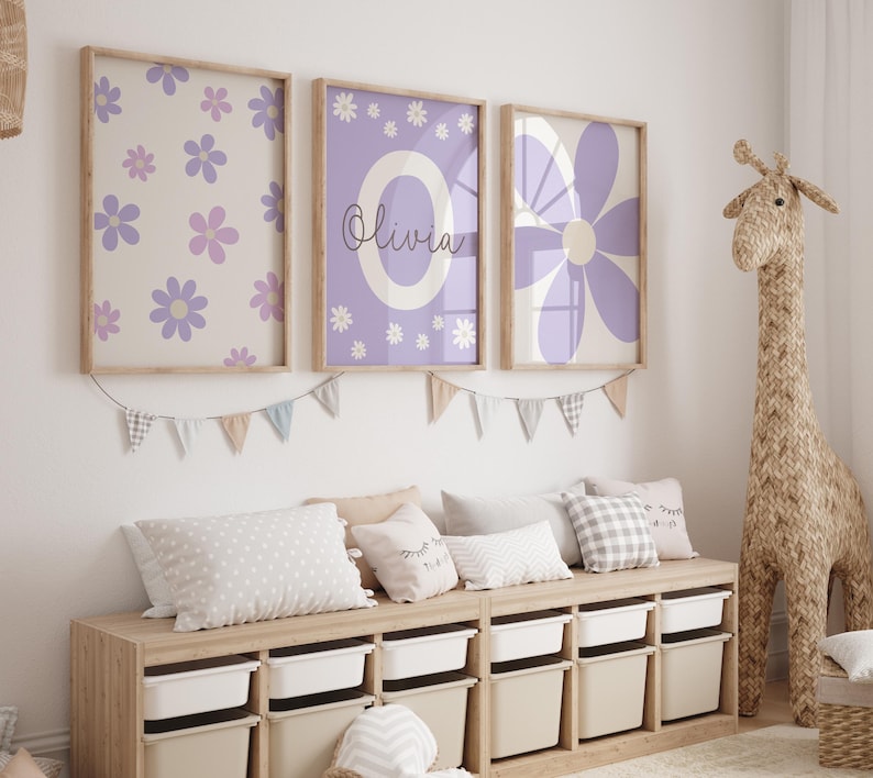 May include: Three framed prints with a purple and white floral design. The middle print has the name "Olivia" written in cursive. The prints are hanging on a white wall above a wooden storage bench with white bins.