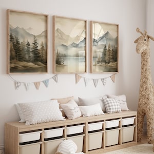 May include: Three framed watercolor landscape prints of mountains and trees hang on a white wall above a wooden storage bench with white drawers. A stuffed giraffe stands next to the bench.