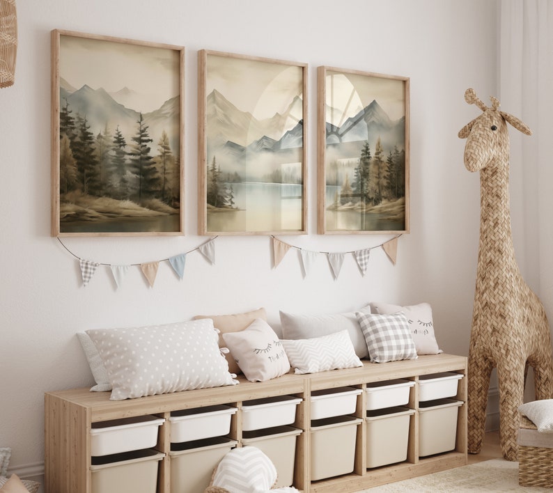 May include: Three framed watercolor landscape prints of mountains and trees hang on a white wall above a wooden storage bench with white drawers. A stuffed giraffe stands next to the bench.
