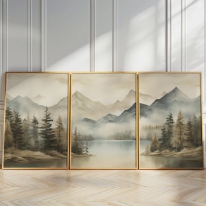 May include: Three framed watercolor paintings depicting a misty mountain landscape with a lake in the foreground. The paintings are in shades of blue, green, and brown, and feature a variety of trees and mountains.