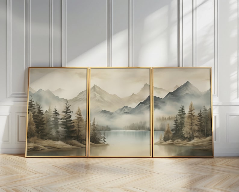 May include: Three framed watercolor paintings depicting a misty mountain landscape with a lake in the foreground. The paintings are in shades of blue, green, and brown, and feature a variety of trees and mountains.