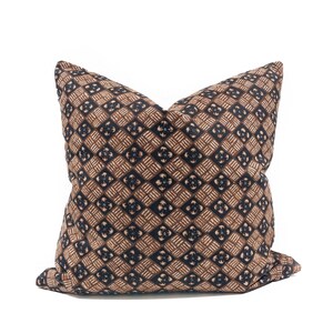 May include: A decorative throw pillow with a geometric pattern. The pillow features a repeating design of brown, tan, and navy blue squares and floral shapes. The pillow is square and appears to be made of fabric.