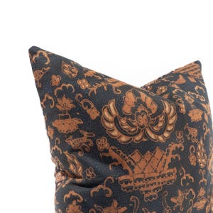 May include: Close-up of a decorative pillow with a dark blue background and a repeating pattern in shades of brown. The pattern includes floral and geometric shapes, creating a textured appearance. The pillow is square and appears to be made of fabric.