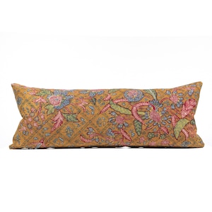 Puede incluir: Cojín lumbar color mostaza con un estampado floral en rosa, azul y verde. El cojín tiene un diseño acolchado y es de forma rectangular. El estampado floral es detallado y cubre toda la superficie del cojín.