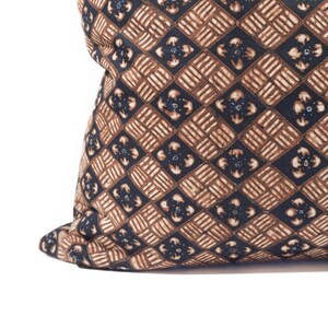 May include: Close-up of a decorative pillow with a repeating geometric pattern. The pattern features brown and navy blue diamond shapes with floral-like accents. The pillow has a soft, textured appearance and is set against a white background.