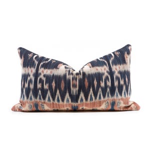 Könnte beinhalten: Ein rechteckiges Zierkissen mit einem blauen, weißen und rostfarbenen Ikat-Muster. Das Kissen hat ein strukturiertes Aussehen und ist für die Inneneinrichtung gedacht. Das Muster zeigt geometrische Formen und Linien. Ca. 60 cm lang.