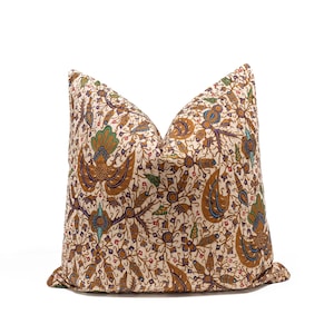 Puede incluir: Un cojín cuadrado con una base de tela color crema y un patrón denso e intrincado de estilo batik. El diseño incluye motivos estilizados de aves y flores en tonos marrón, beige, verde azulado y verde, con líneas finas de color marrón oscuro.