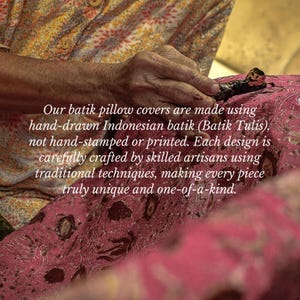 May include: A person's hand using a tool to apply wax to a pink batik fabric. The fabric has a floral pattern. The text says the pillow covers are hand-drawn Indonesian batik.