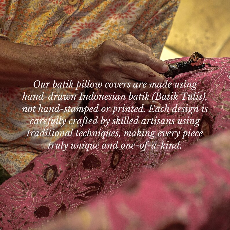 May include: A person's hand using a tool to apply wax to a pink batik fabric. The fabric has a floral pattern. The text says the pillow covers are hand-drawn Indonesian batik.