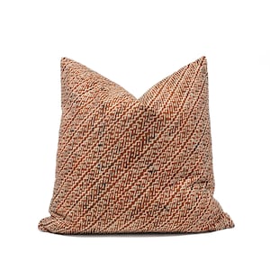 Op de afbeelding: Een vierkant decoratief kussen met een diagonaal patroon in bruin-, crème- en zwarttinten. Het kussen heeft een textuur en is waarschijnlijk gemaakt van stof. Het kussen is een woondecoratie-artikel.