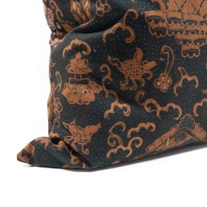 May include: Close-up of a dark pillow with a repeating pattern in brown and black. The pattern includes stylized birds, clouds, and other shapes. The pillow is folded over, showing the fabric's texture.