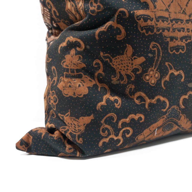 May include: Close-up of a dark pillow with a repeating pattern in brown and black. The pattern includes stylized birds, clouds, and other shapes. The pillow is folded over, showing the fabric's texture.
