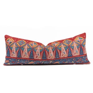 Può includere: Un cuscino lombare rettangolare caratterizzato da uno sfondo rosso vivace con un motivo ripetuto di forme triangolari geometriche blu, rosa e gialle. La sezione inferiore presenta una fascia orizzontale con intricati motivi floreali e paisley blu.