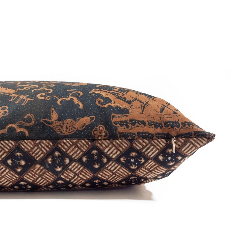 May include: Decorative pillow with a brown and black batik pattern. The pillow features a repeating geometric design on the bottom and a detailed, ornate pattern on the top. A zipper is visible on the side.