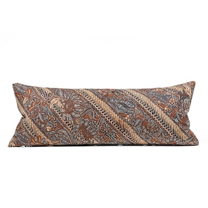 Può includere: Un lungo cuscino rettangolare con un motivo batik marrone, blu e beige. Il tessuto presenta un design dettagliato di forme floreali e geometriche disposte a strisce diagonali. Il cuscino è un elemento decorativo per un letto o un divano.