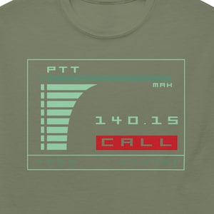 May include: Olive green t-shirt with a retro-style graphic. The graphic features a digital display with the text "PTT," "MAX," "140.15," and "CALL." The display is in shades of green and red, creating a vintage aesthetic.