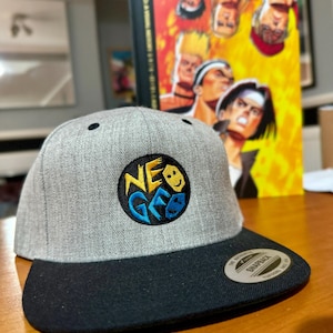 May include: A gray and black baseball cap with a black and yellow embroidered logo that says "NEO GEO".