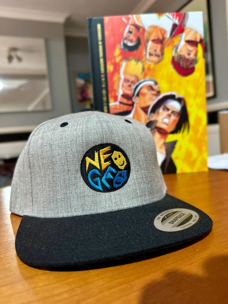 May include: A gray and black baseball cap with a black and yellow embroidered logo that says "NEO GEO".