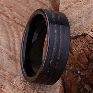 May include: A black tungsten carbide ring with a thin red and silver inlay. The ring has a polished finish and a beveled edge.
