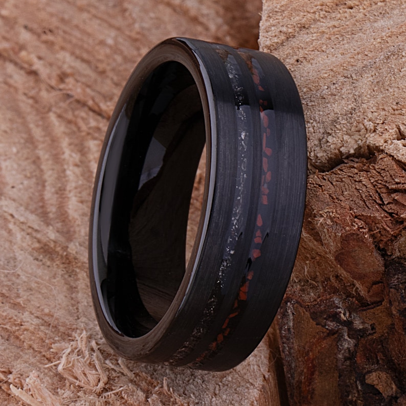 May include: A black tungsten carbide ring with a thin red and silver inlay. The ring has a polished finish and a beveled edge.