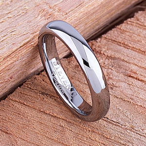 May include: A silver tungsten carbide ring with a polished finish. The ring is engraved with the words "Steven G Tungsten".