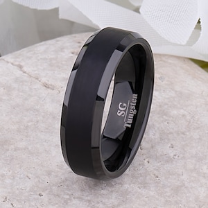May include: A black tungsten ring with a beveled edge and a brushed finish. The ring has the inscription "SG Tungsten" on the inside.