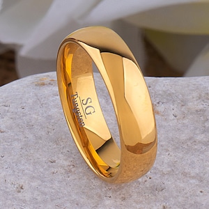 May include: A gold tungsten ring with a bevelled edge and the inscription "SG Tungsten" on the inside.